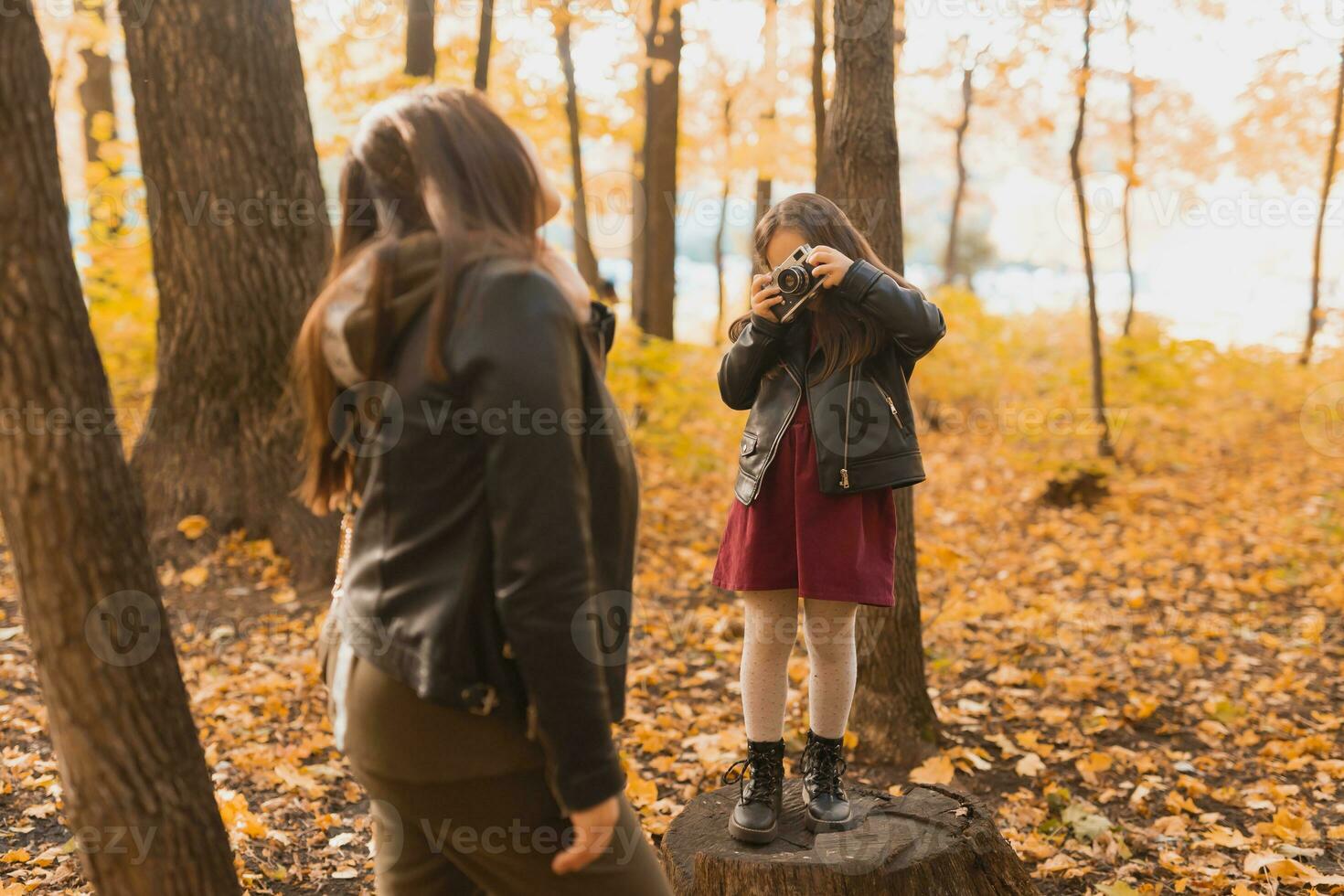 Child girl photographer takes pictures of a mother in the park in autumn. Hobbies, photo art and leisure concept.