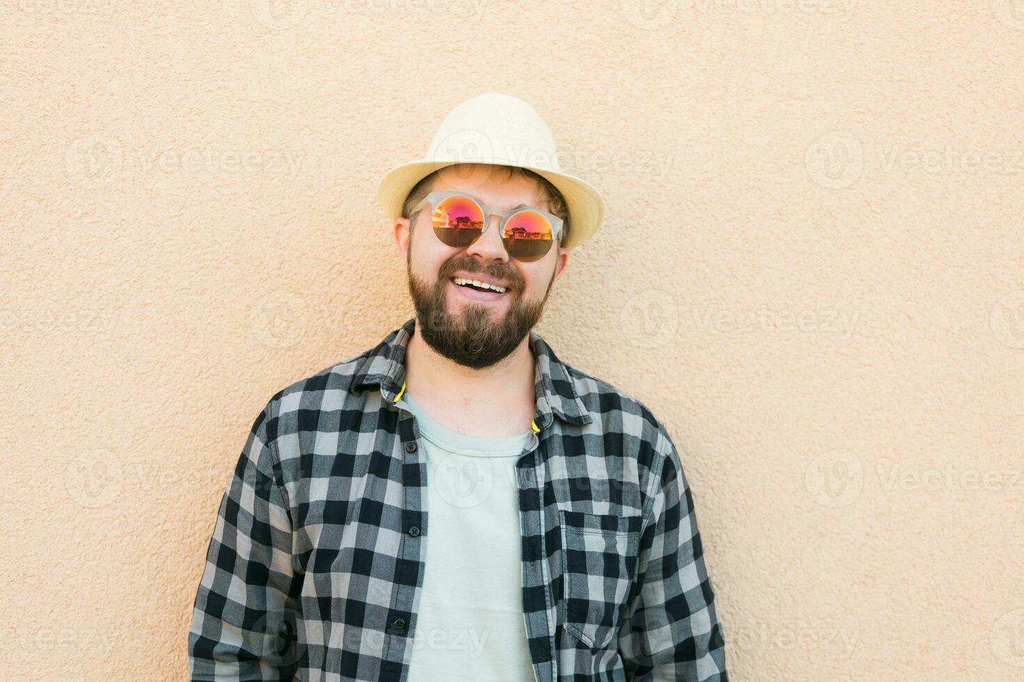 Portrait handsome man wearing summer hat and sunglasses and plaid shirt smiling happy near wall - travel vacations and summer holiday concept photo