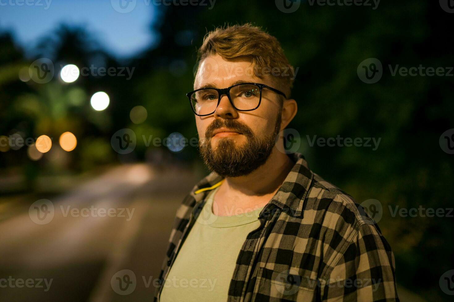 Portrait of man standing in night city street with bokeh street lights in background. Confident lonely guy. Close-up portrait photo
