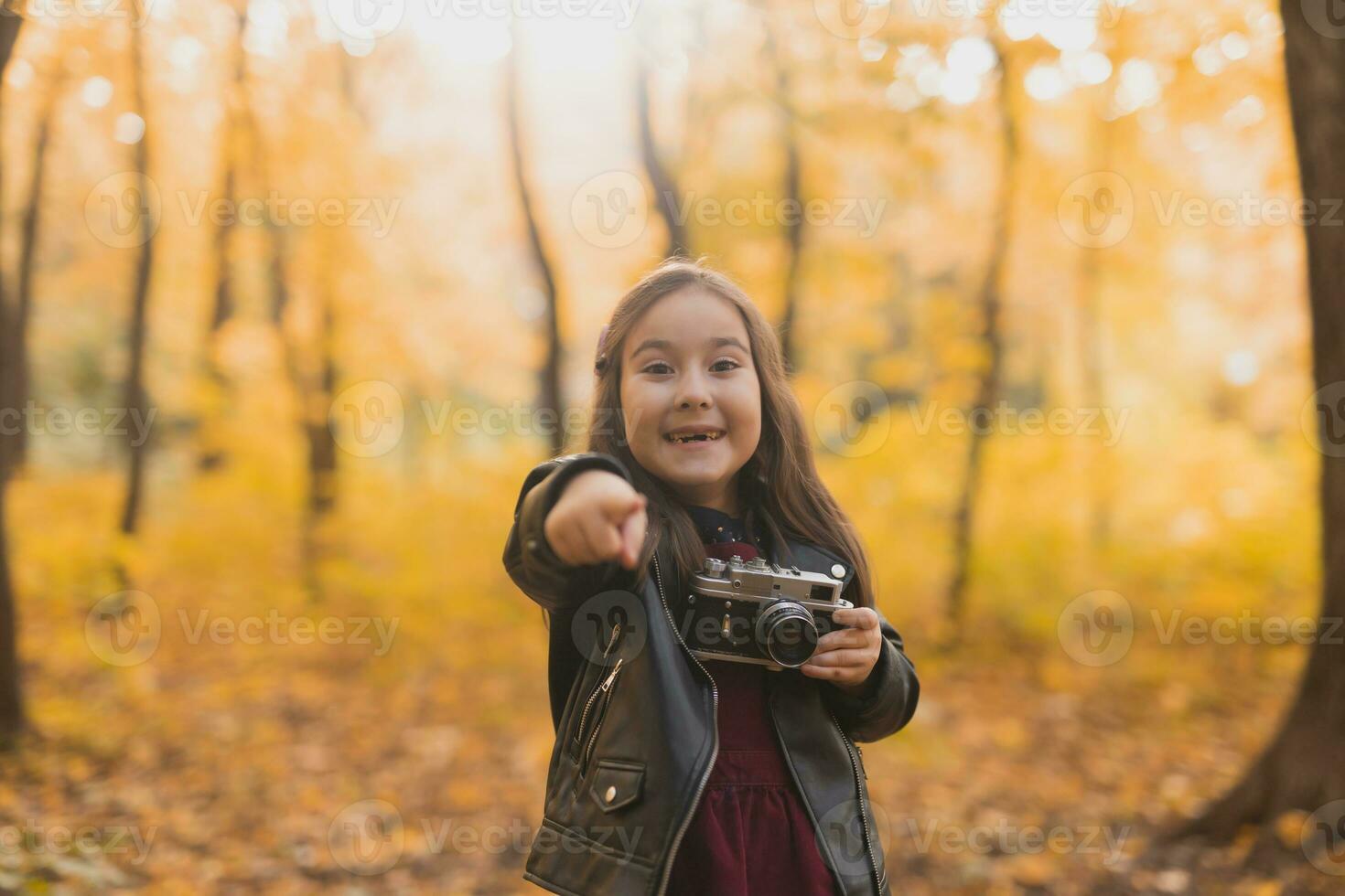 Surprised child girl using an old-fashioned camera in autumn nature. Photographer, fall season and emotions concept. photo