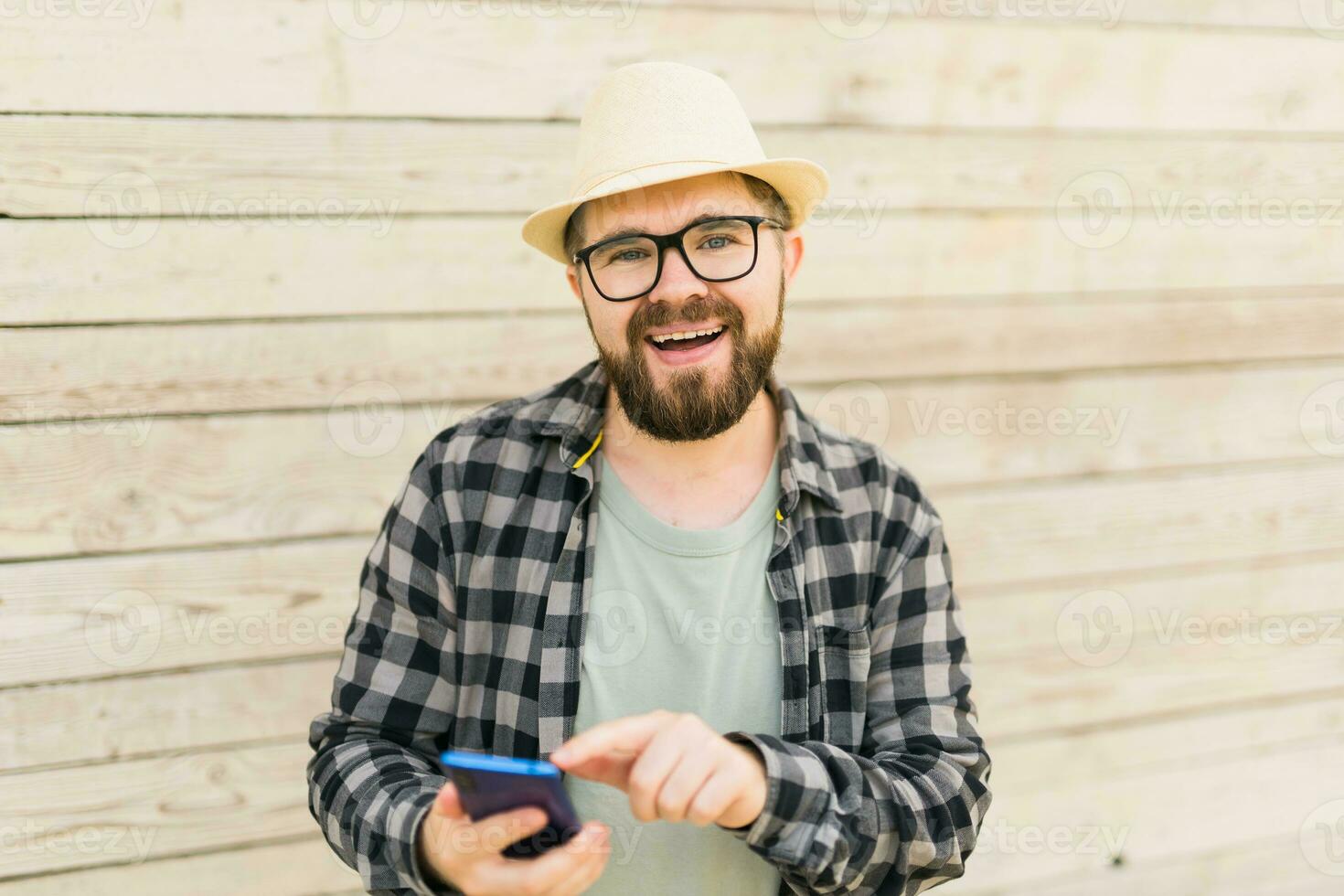Smiling male tourist use smartphone during summer city break over wooden wall - technologies and social media app concept photo