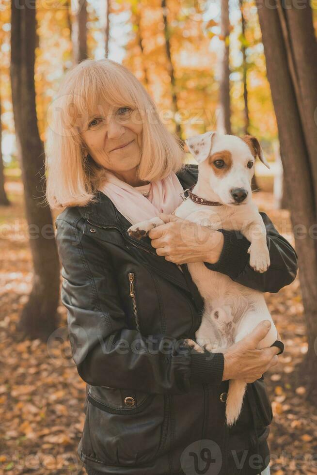 Senior smiling woman hugging her dog in autumn park. Active aging and pet concept. photo