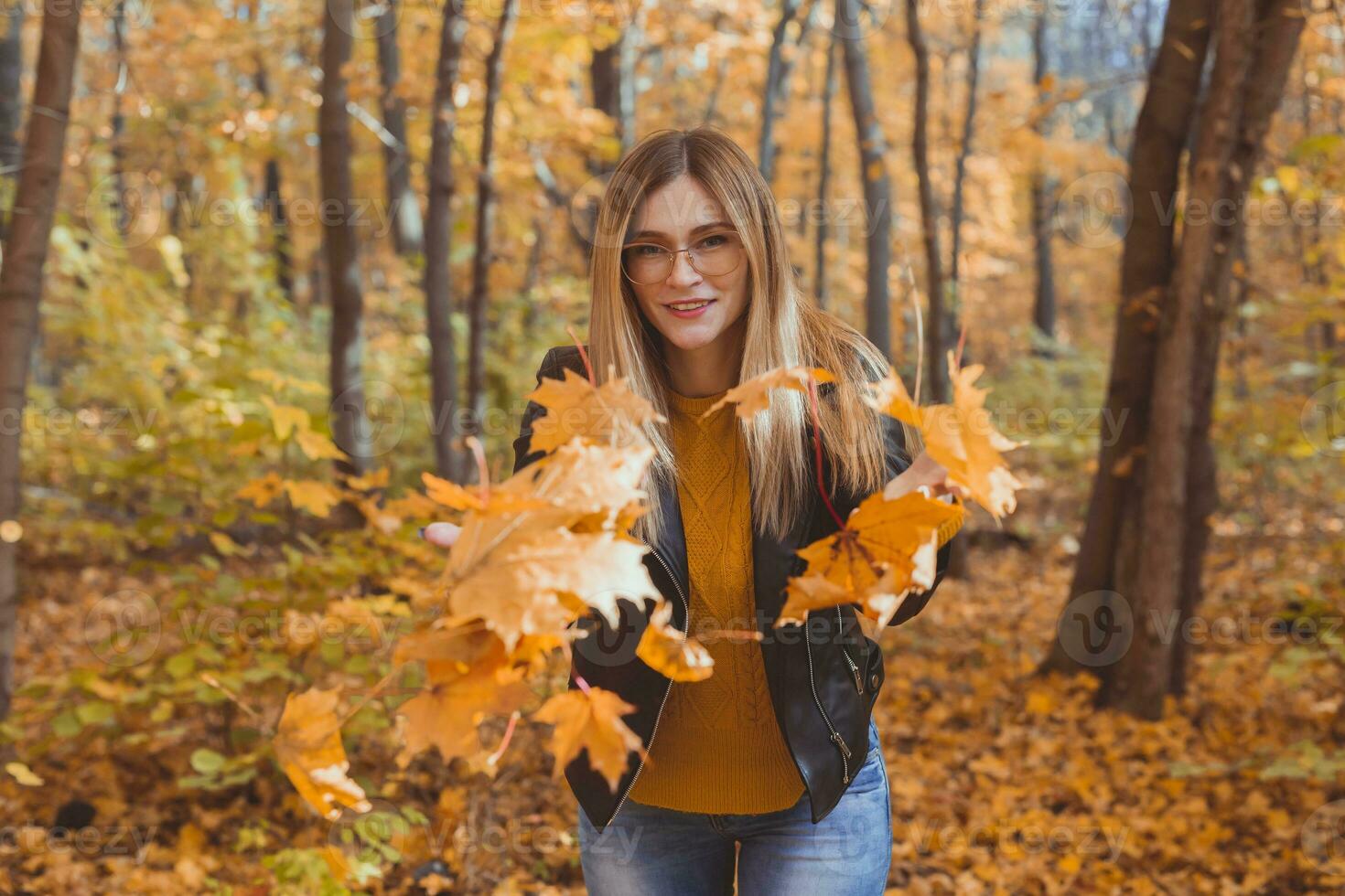 Happy laughing young woman throwing leaves in autumn park. Fall season photo