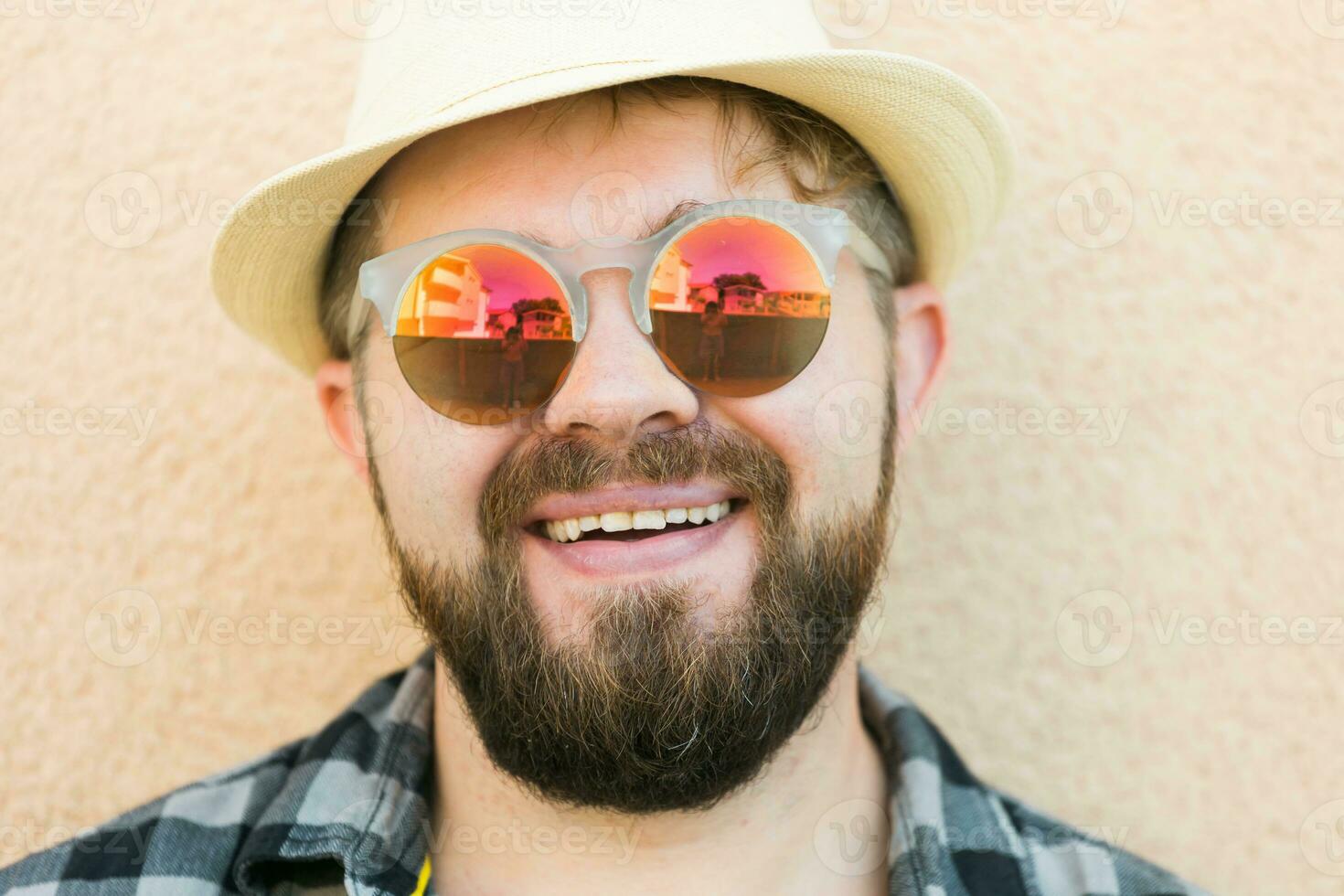 Portrait handsome man wearing summer hat and sunglasses and plaid shirt smiling happy near wall - travel vacations and summer holiday concept photo