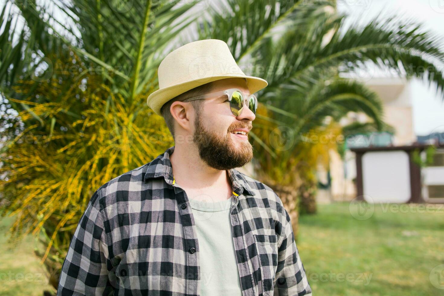 Laughing attractive man wearing hat over palm tree background with copy space - emotion and vacation travel holidays concept photo