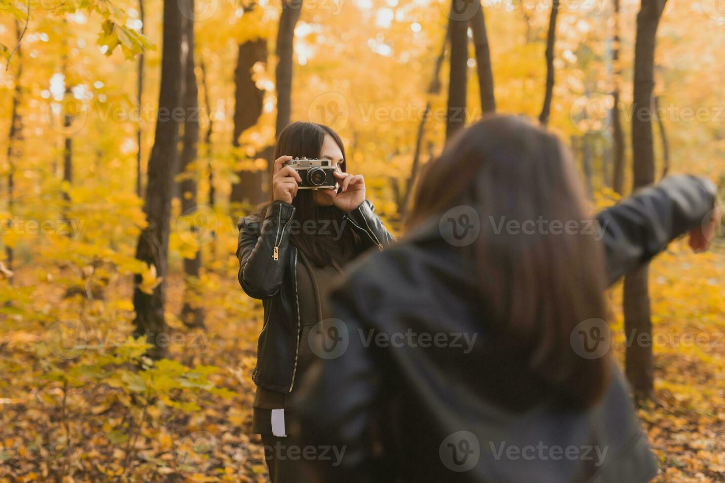 Mother taking picture her charismatic daughter on retro camera in autumn park. Hobbies and leisure concept. photo