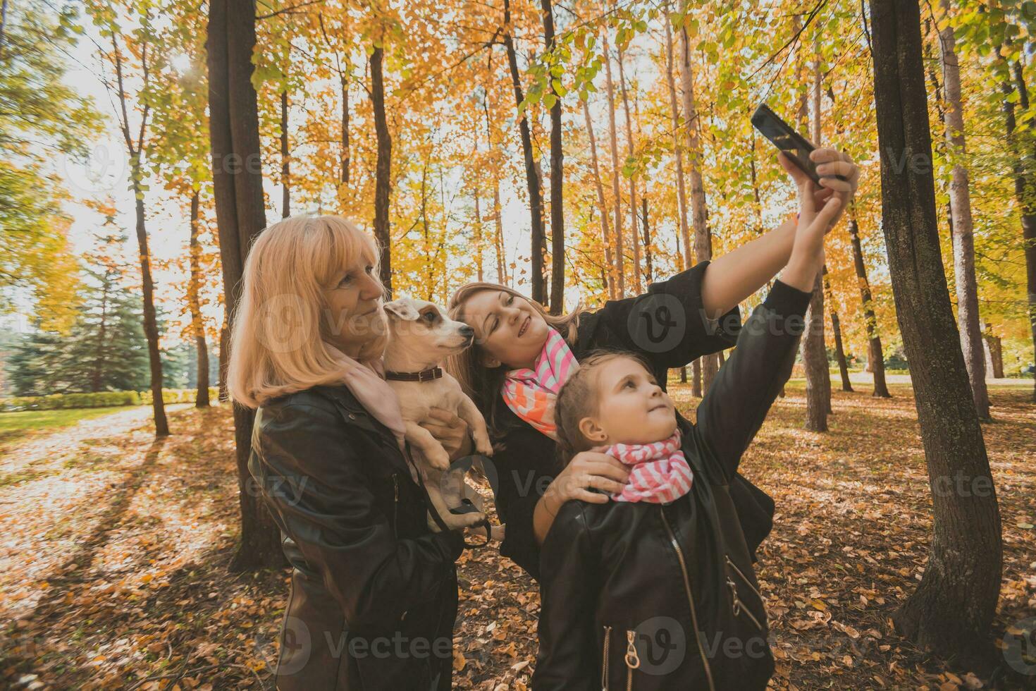 Three generations of women and dog feel fun look at camera posing for self-portrait picture together, funny excited child, mom and grandmother have fun enjoy weekend take selfie on gadget in autumn photo