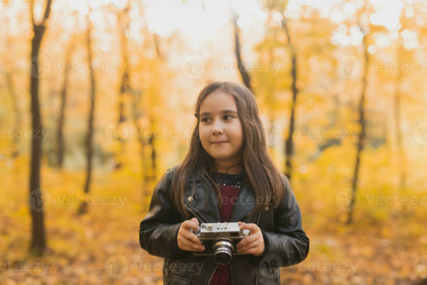 A little girl take a photo with old retro camera in autumn nature. Leisure and hobby concept.