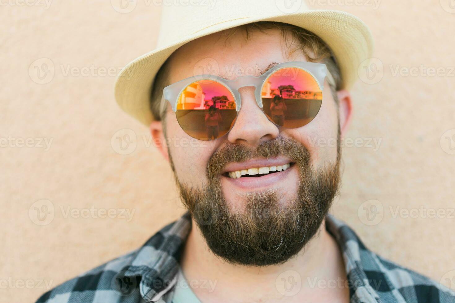 Portrait handsome man wearing summer hat and sunglasses and plaid shirt smiling happy near wall - travel vacations and summer holiday concept photo