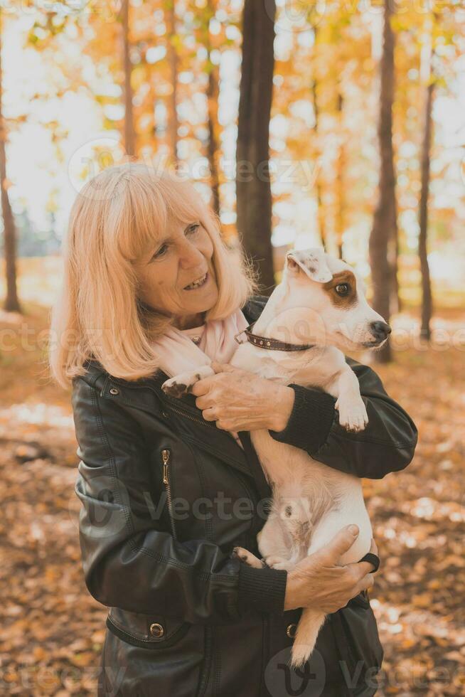 Senior smiling woman hugging her dog in autumn park. Active aging and pet concept. photo