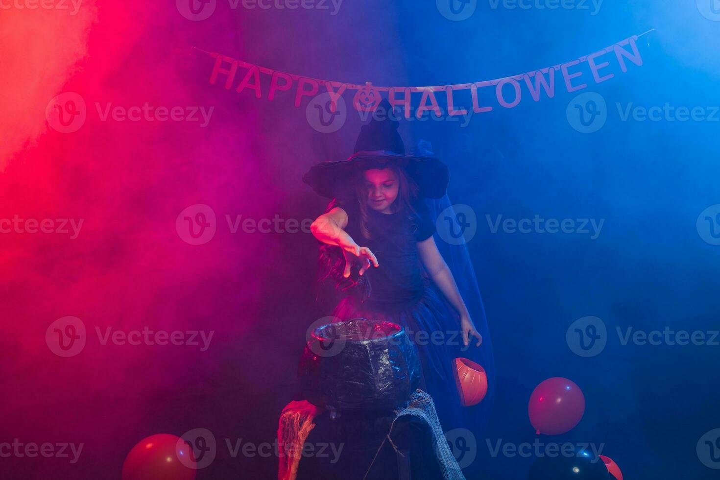 Child girl witch preparing a potion in the cauldron at halloween holidays. photo