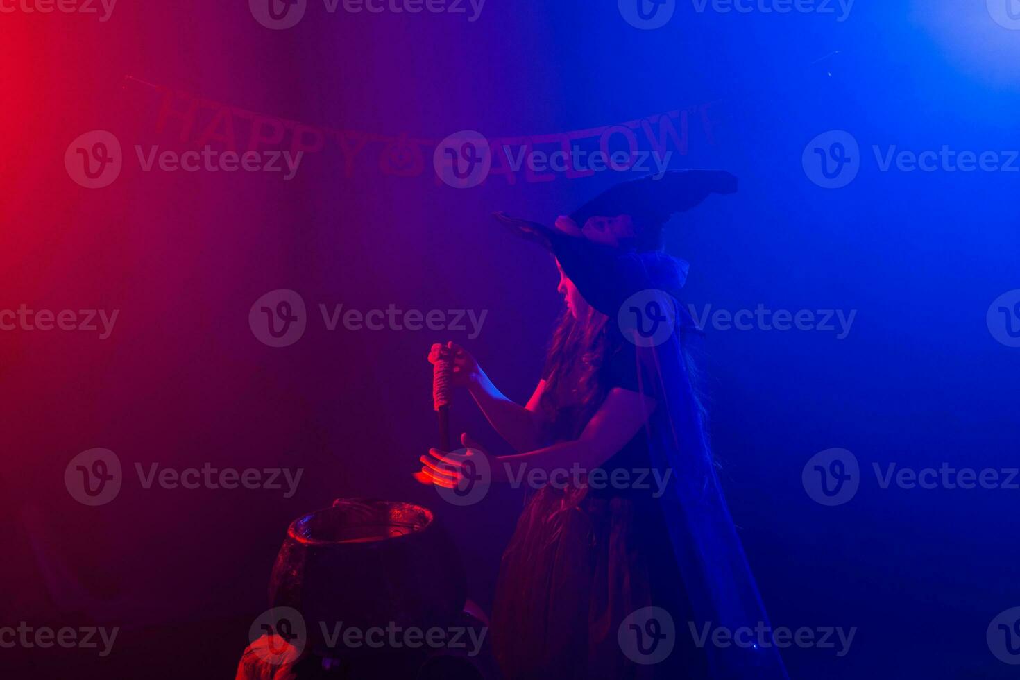 Child girl witch preparing a potion in the cauldron at halloween holidays. Copy space. photo