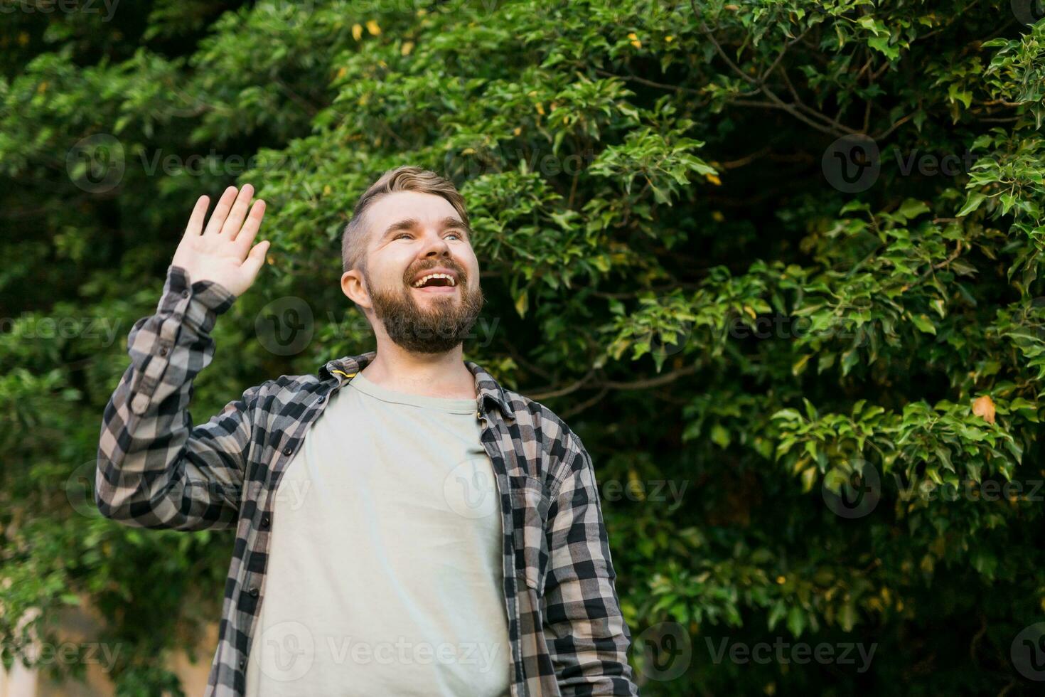 Side view of delighted male standing outdoors and waving hand to his friend. He is joyful to meet his acquainted by chance. Copy space and place for advertising photo