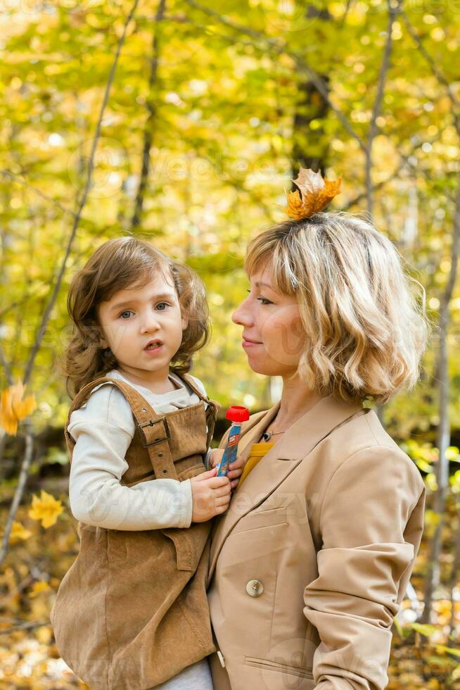 Young mother with her little daughter in an autumn park. Fall season, parenting and children concept. photo