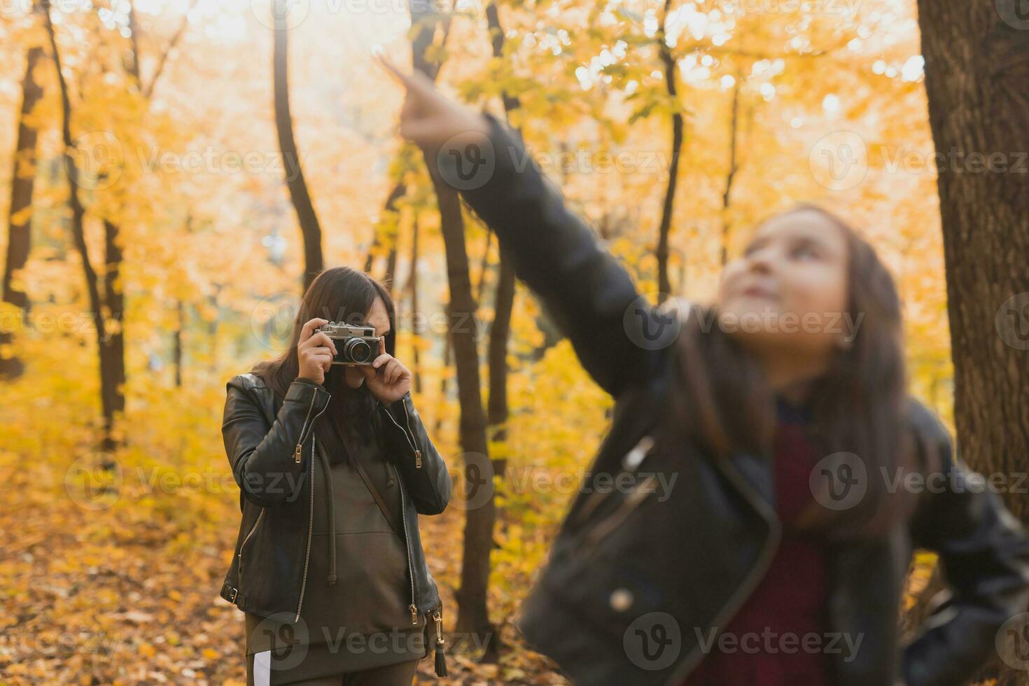 Mother photographer takes pictures of a her daughter in the park in autumn. Hobbies, photo art and leisure concept.