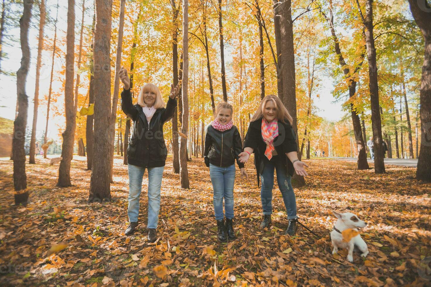 Grandmother and mother with granddaughter throw up fall leaves in autumn park and having fun. Generation, leisure and family concept. photo