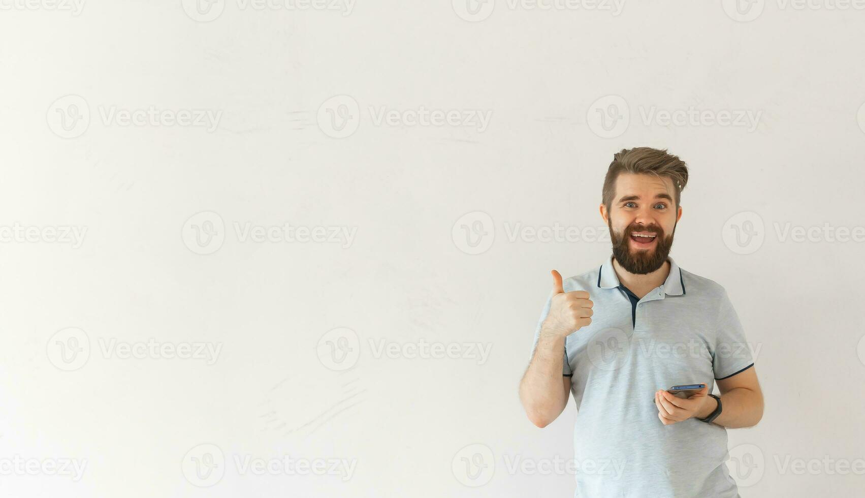 Funny caucasian man holding smartphone and thumbs up gesture isolated over white background copy space. Social networks and gadget concept photo