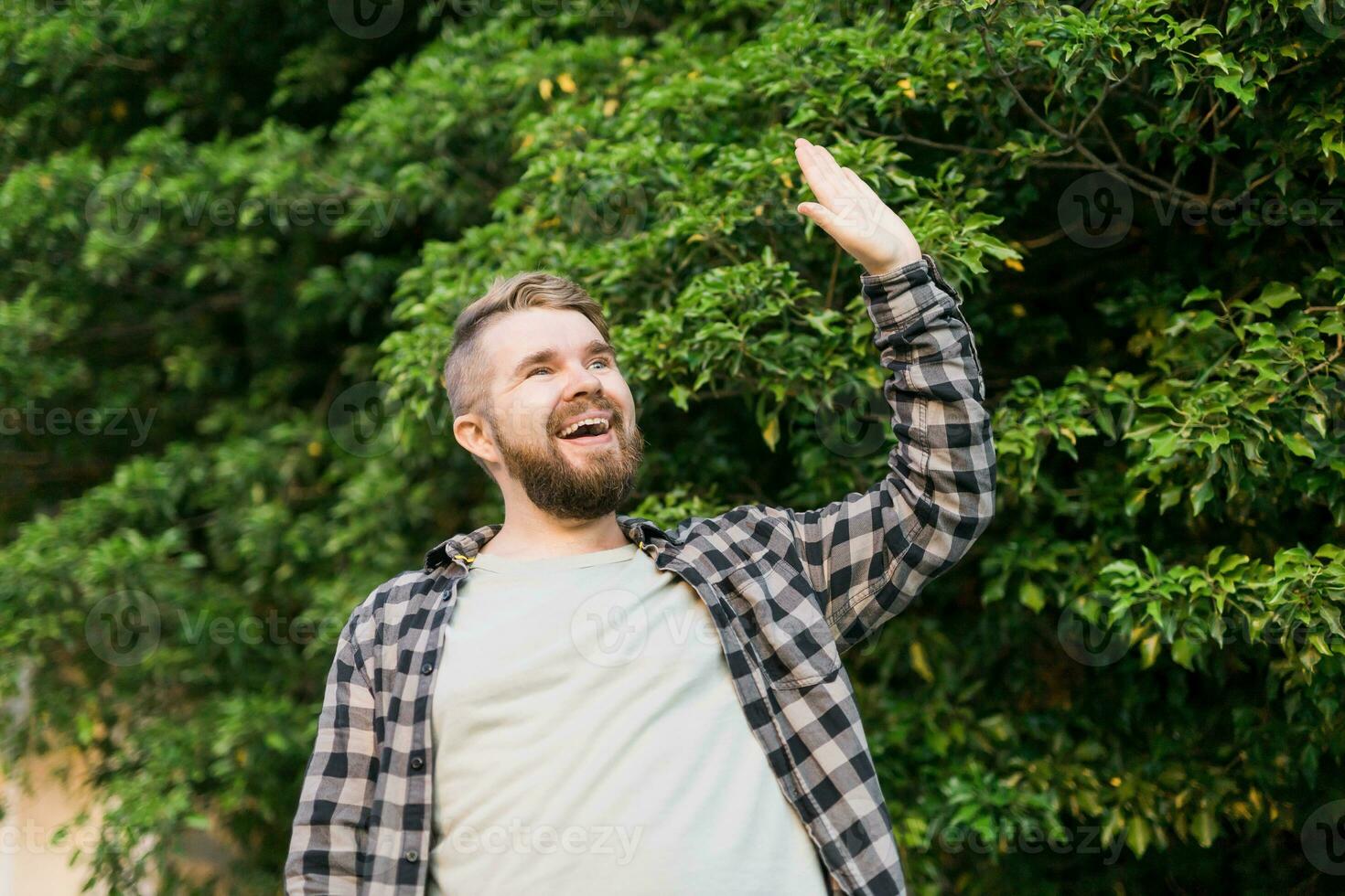 Side view of delighted male standing outdoors and waving hand to his friend. He is joyful to meet his acquainted by chance. photo