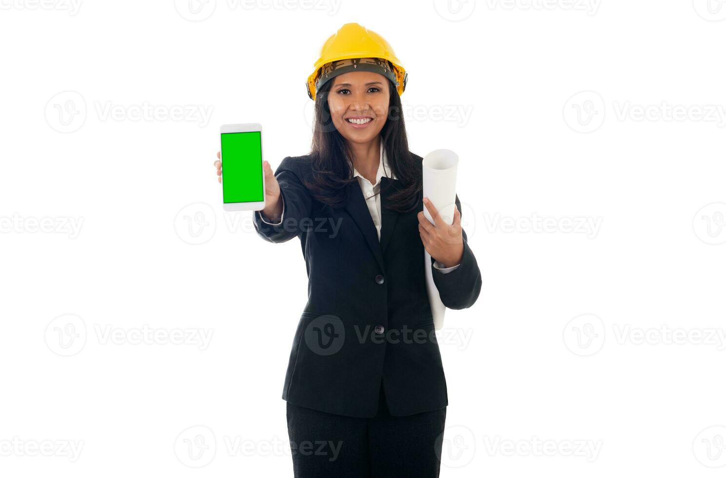portrait of mixed race asian engineer woman with helmet holding blueprints and showing green screen mobile phone isolated white background photo