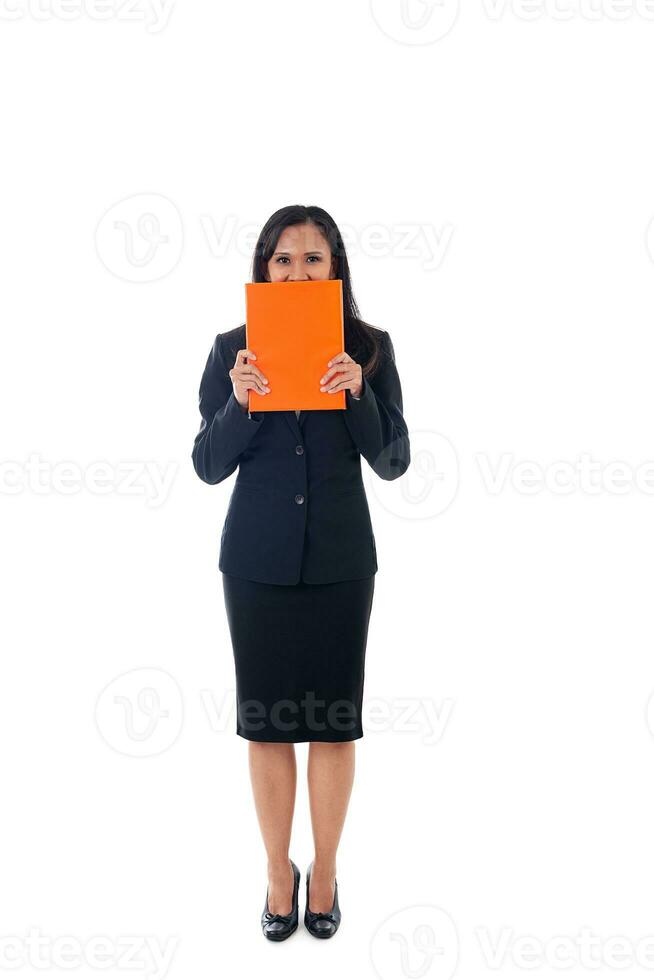 Smiling asian modern business woman holding book and hidden behind the book, looking at camera, full length portrait isolated on white background. photo