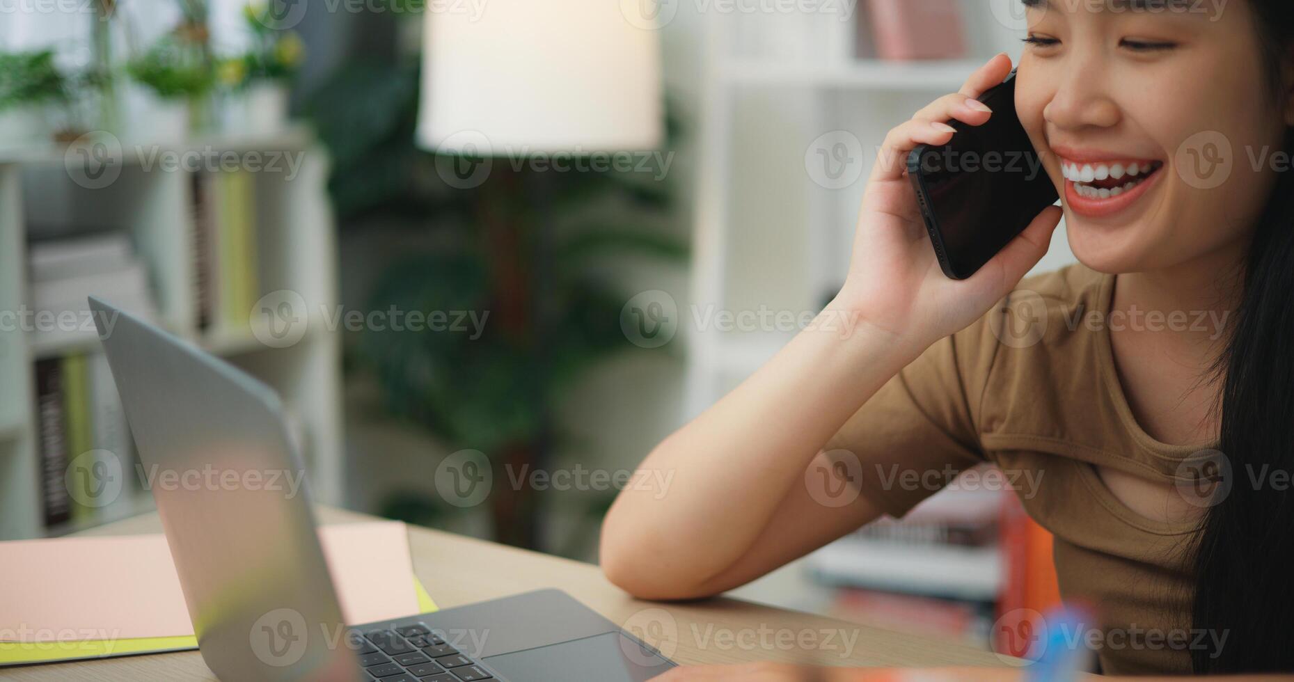 Young Asian woman working with a laptop on a desk while talking on phone photo