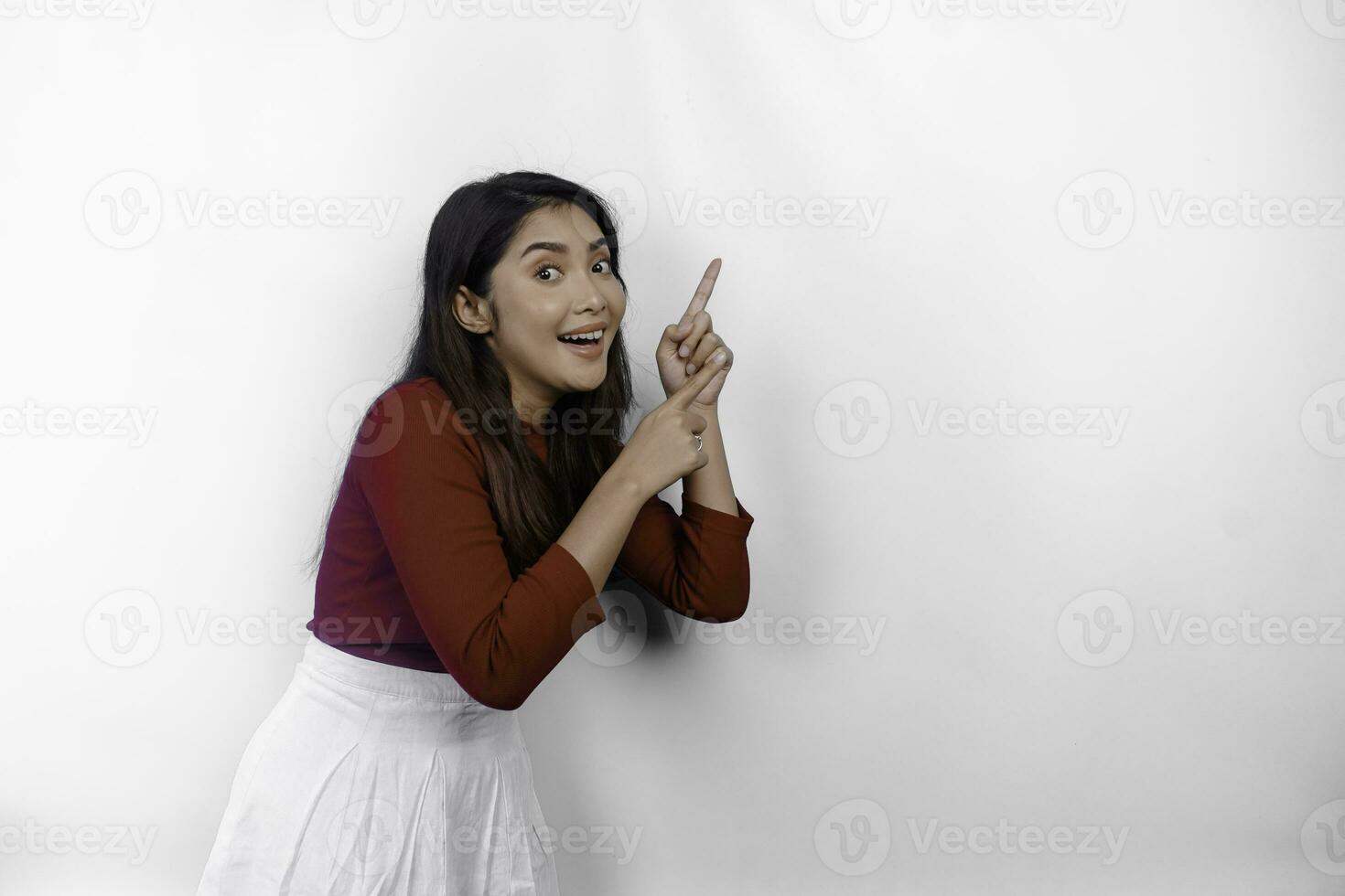 Excited Asian woman wearing red t-shirt, pointing at the copy space on top of her, isolated by white background photo