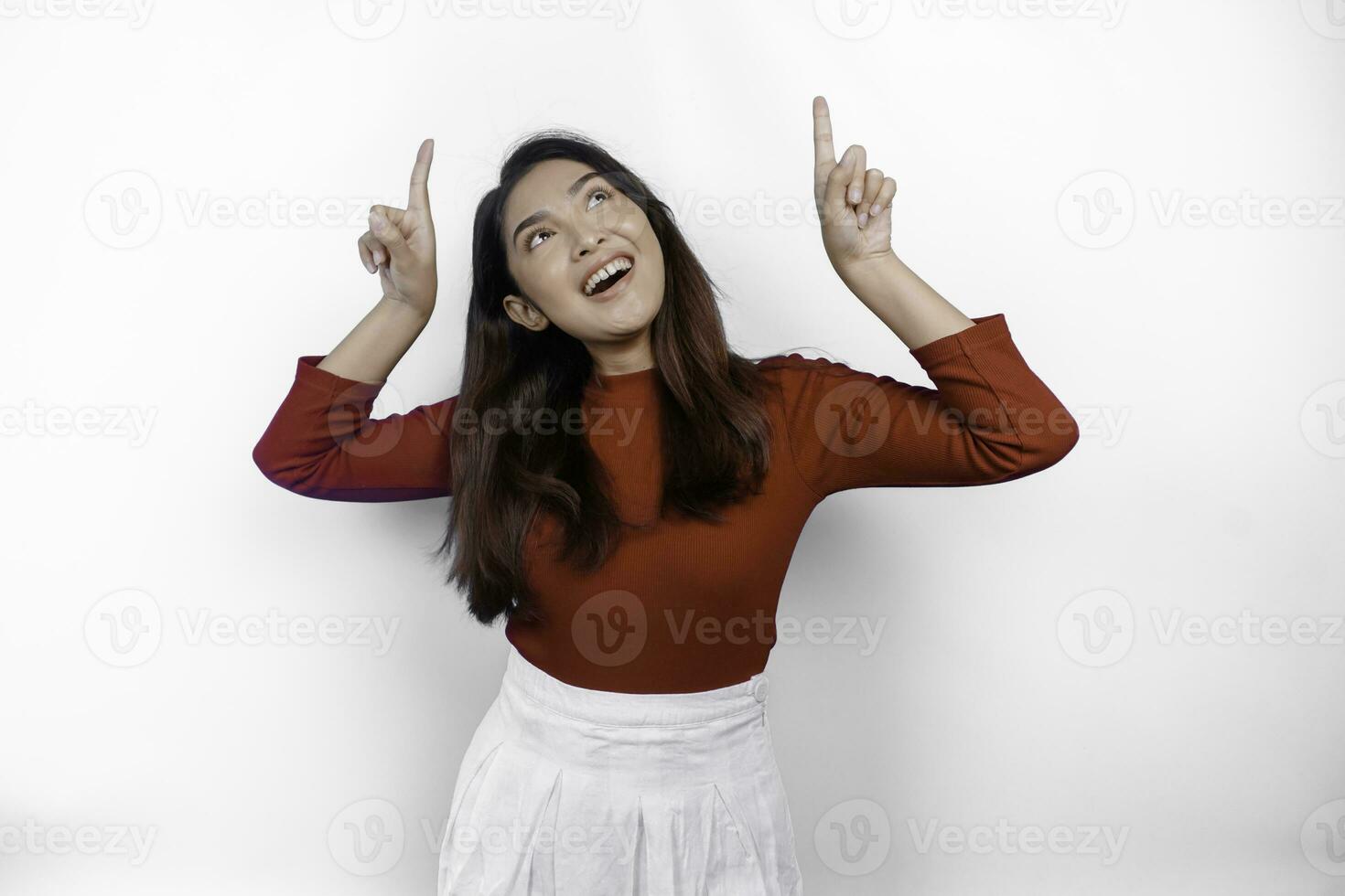 Excited Asian woman wearing red t-shirt, pointing at the copy space on top of her, isolated by white background photo