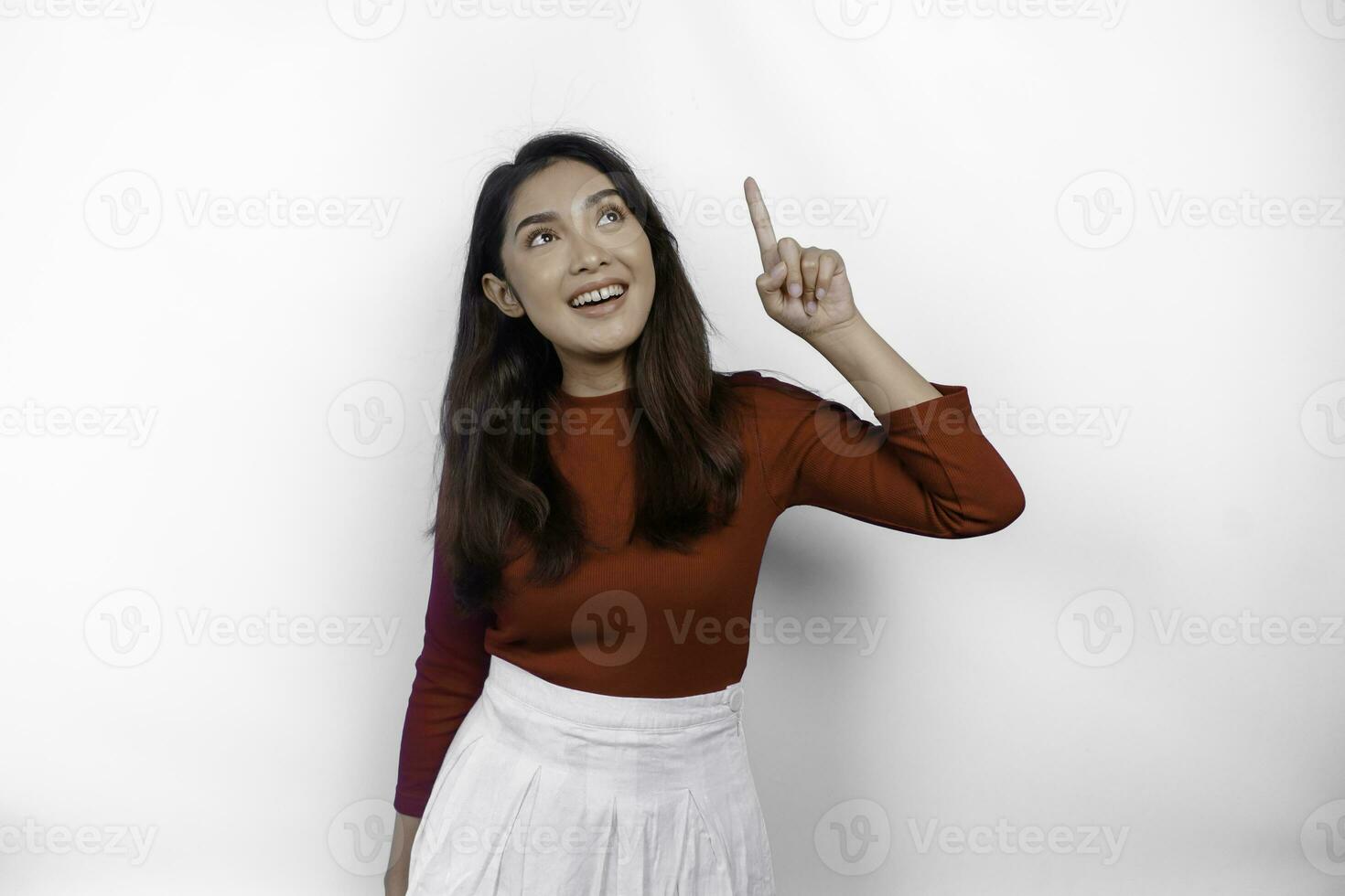 Excited Asian woman wearing red t-shirt, pointing at the copy space on top of her, isolated by white background photo