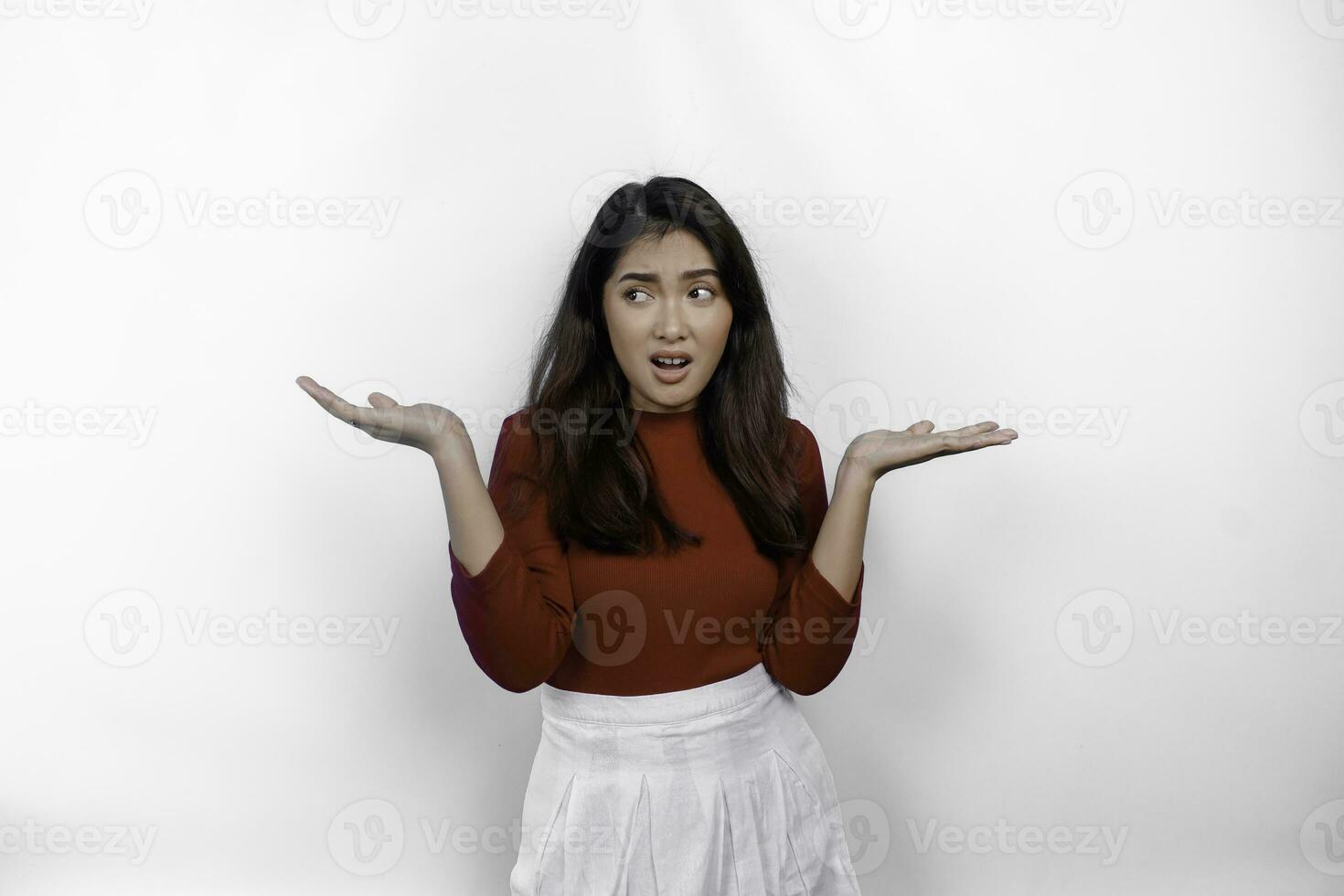 un pensativo joven asiático mujer es vistiendo rojo camiseta mira confuso Entre elecciones, aislado por blanco antecedentes foto