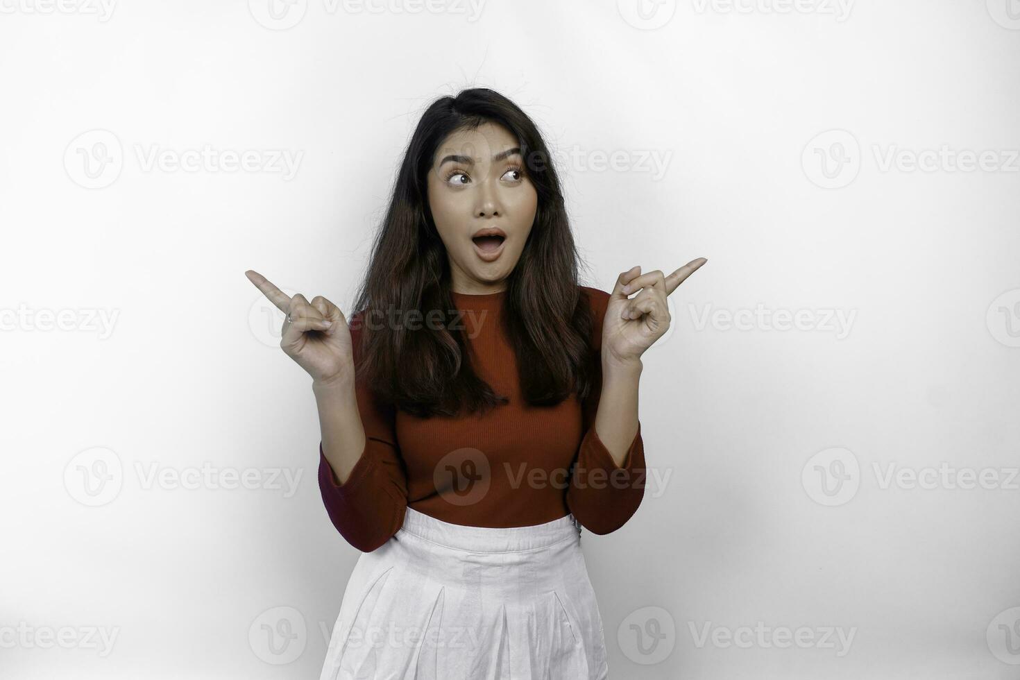 Shocked Asian woman wearing red t-shirt, pointing at the copy space on beside her, isolated by white background photo