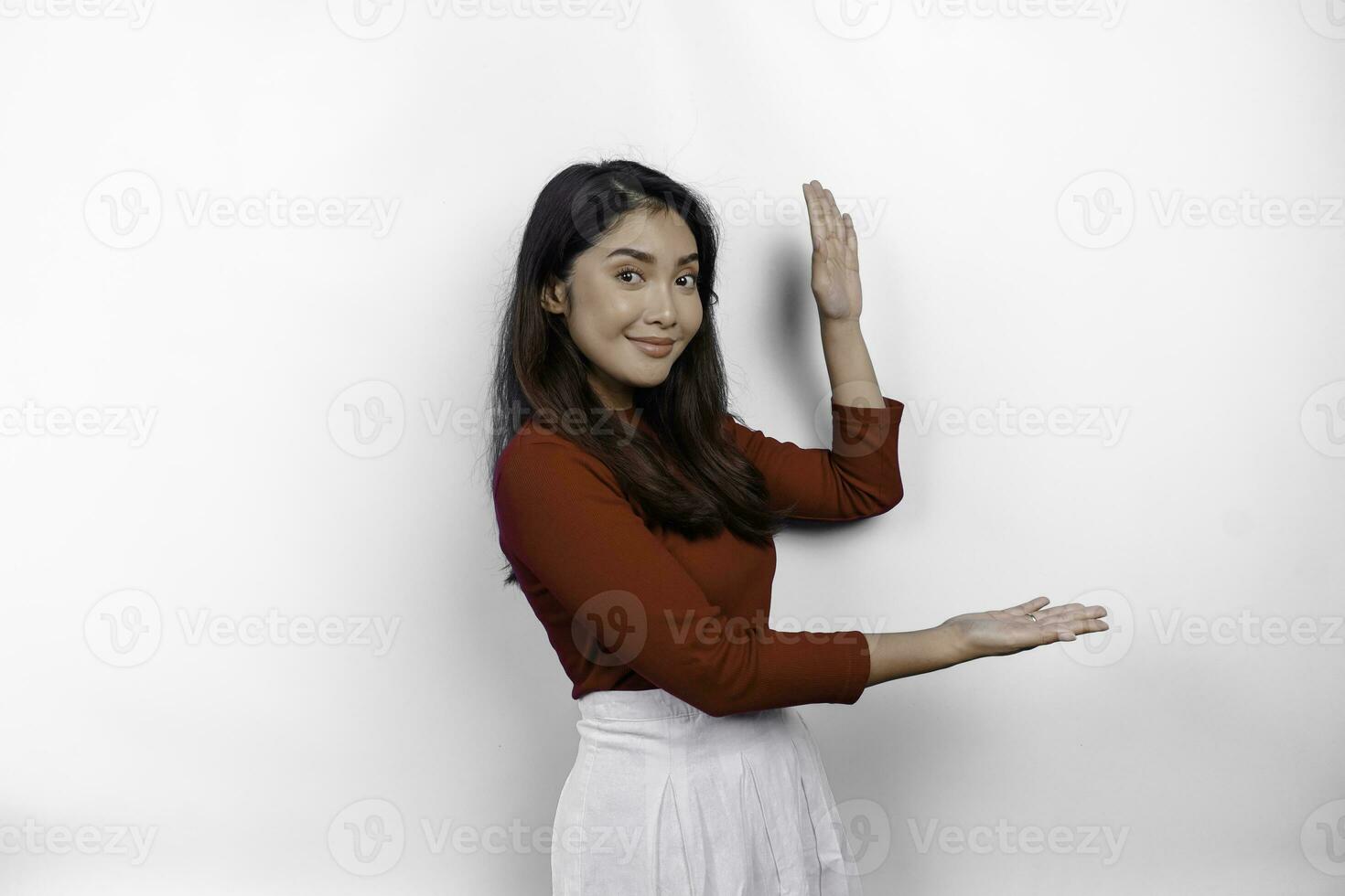 Excited Asian woman wearing red t-shirt, pointing at the copy space beside her, isolated by white background photo