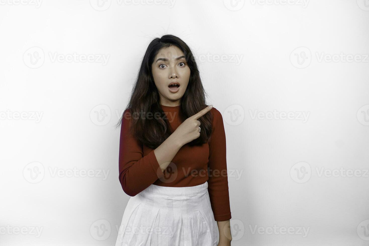 Shocked Asian woman wearing red t-shirt, pointing at the copy space on beside her, isolated by white background photo