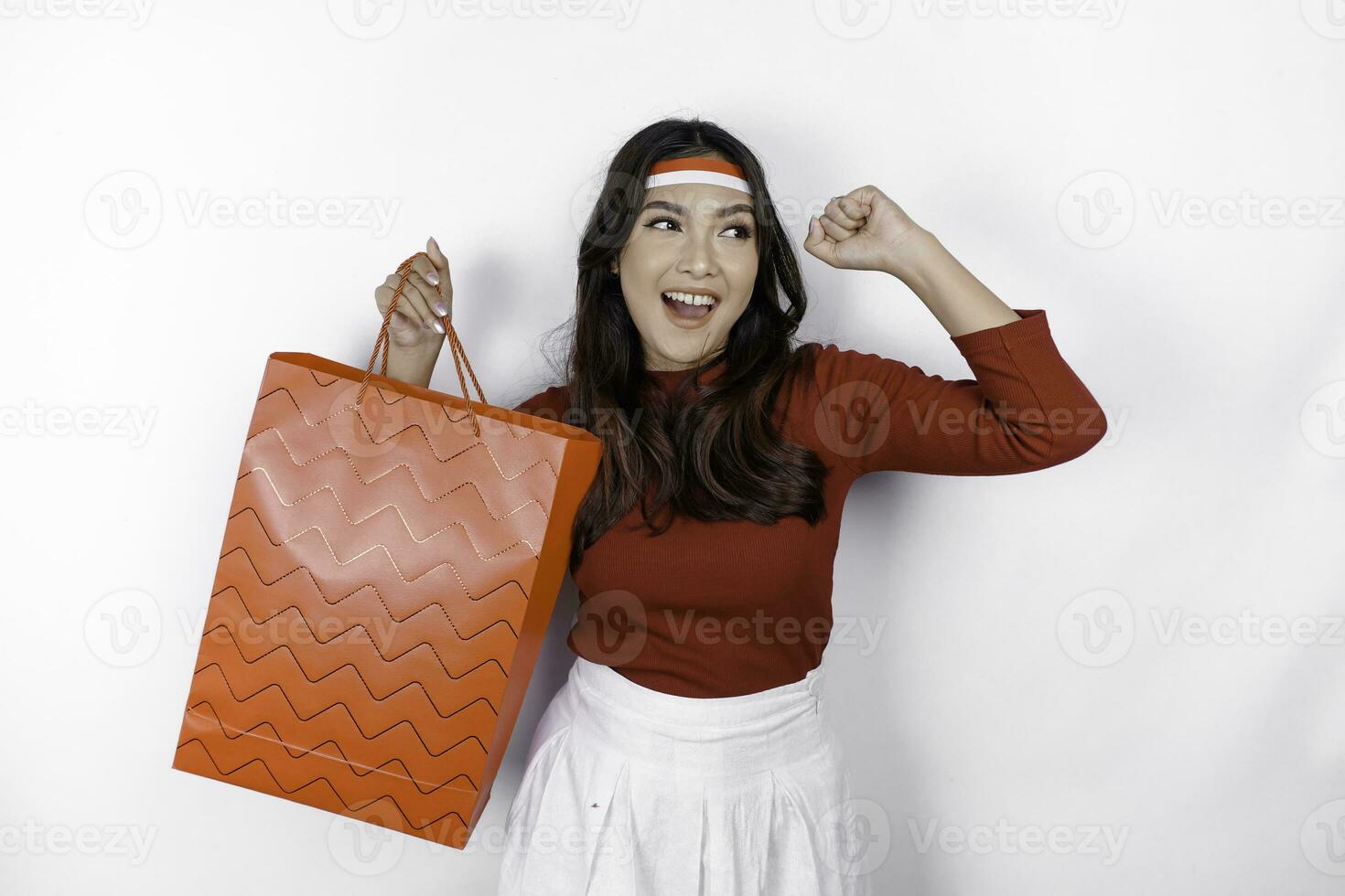 contento joven asiático mujer es sonriente mientras trayendo compras bolsa, aislado en blanco antecedentes. indonesio independencia día rebaja concepto foto