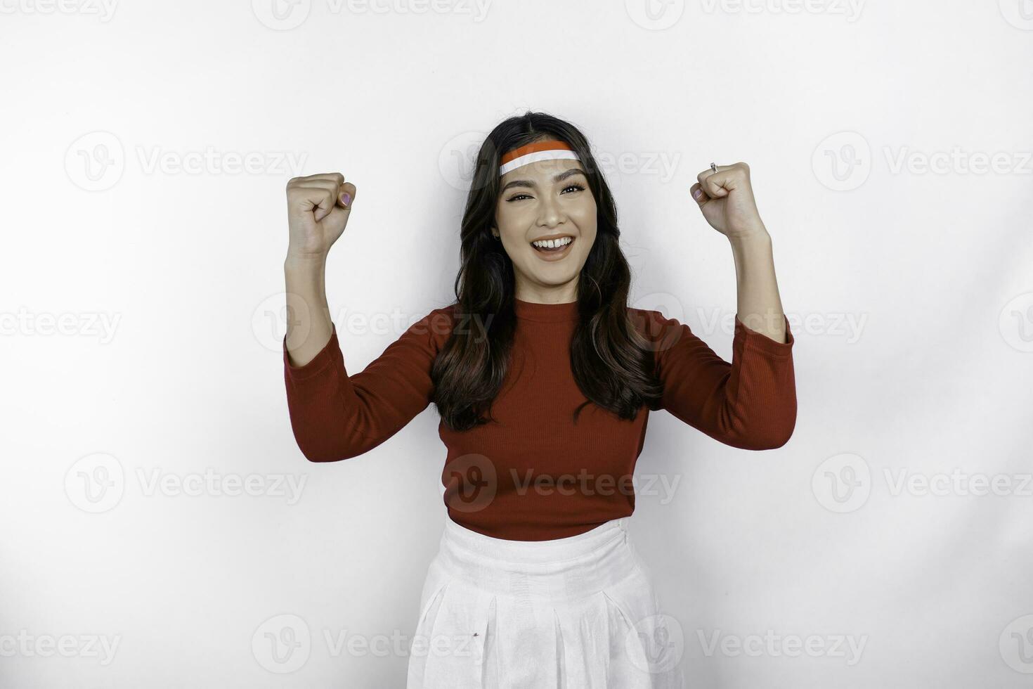 A young Asian woman with a happy successful expression wearing red top and flag headband isolated by white background. Indonesia's independence day concept. photo