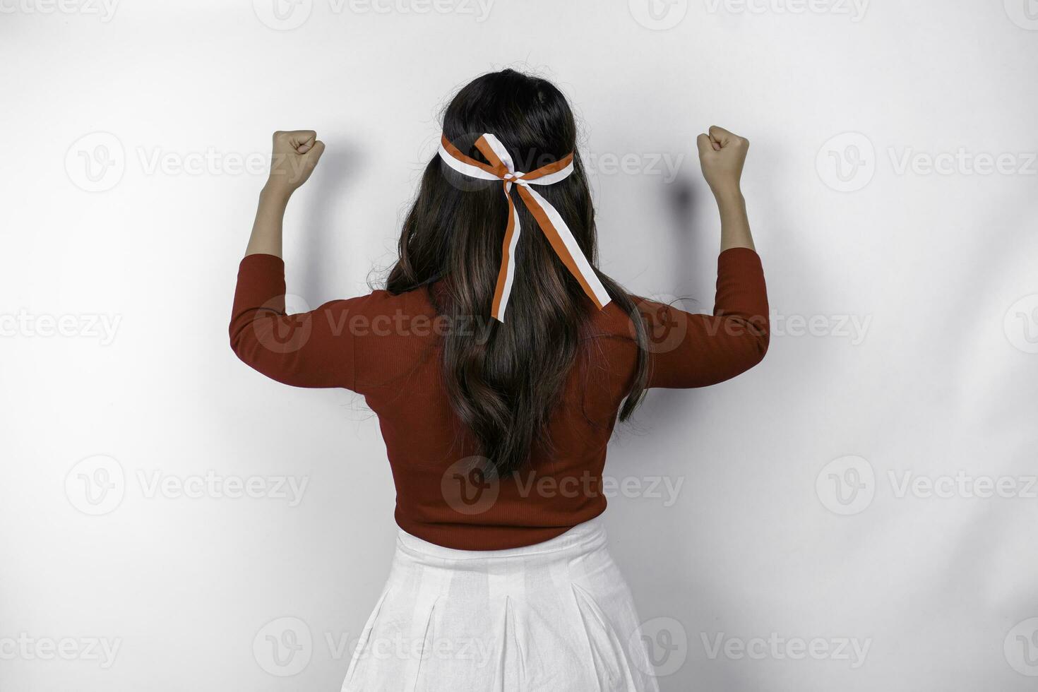 Back view of a young Asian woman with a happy successful gesture wearing red top and flag headband isolated by white background. Indonesia's independence day concept. photo