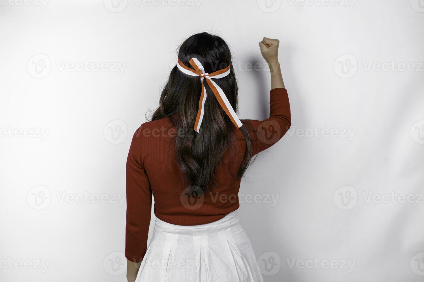 Back view of a young Asian woman with a happy successful gesture wearing red top and flag headband isolated by white background. Indonesia's independence day concept. photo