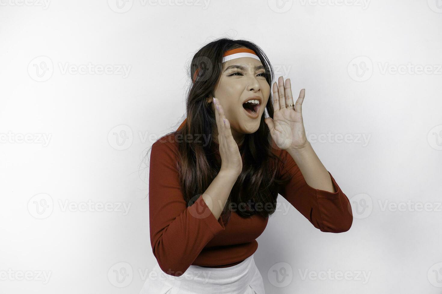 Young beautiful woman wearing a red top shouting and screaming loud with a hand on her mouth. Indonesia's independence day concept. photo
