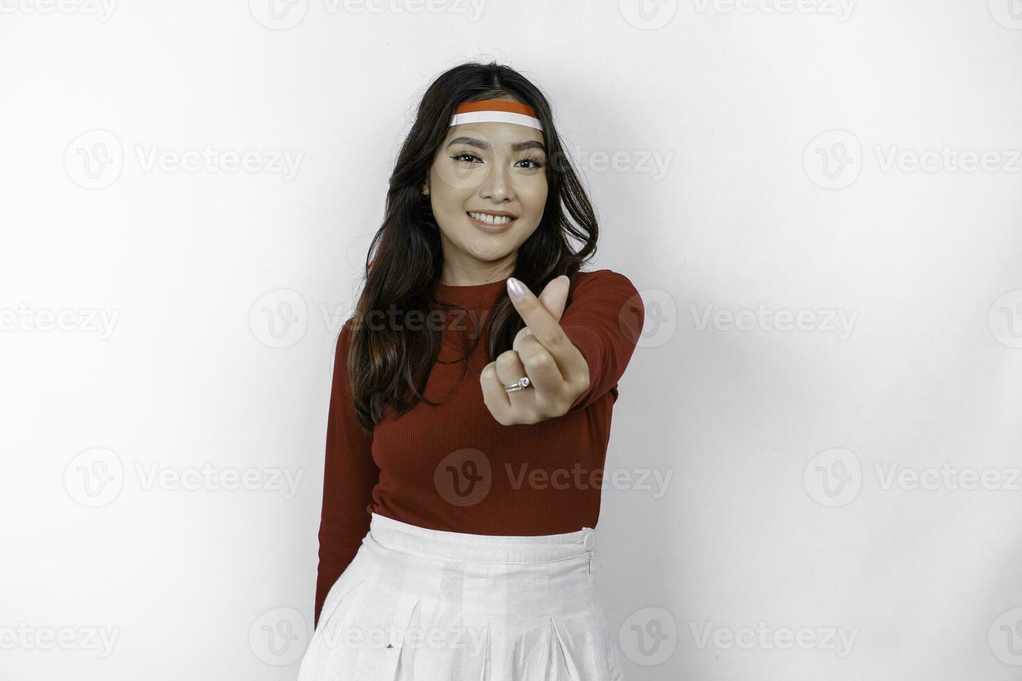 A young Asian woman wearing a red top feels nationalism, shapes heart gesture expresses her love for Indonesia. Indonesia's independence day concept. photo