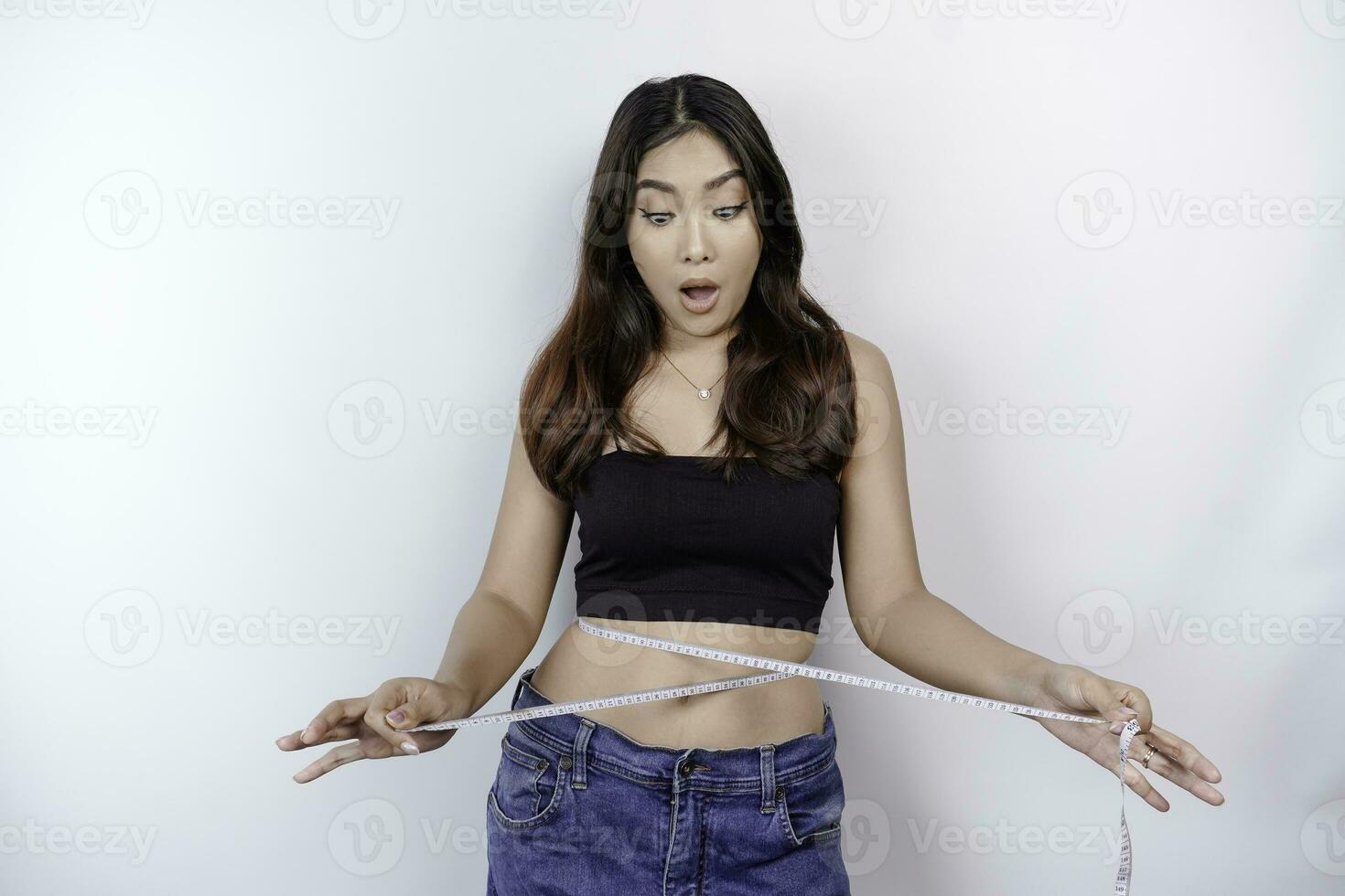 Diet lifestyle concept. Shocked Asian girl measuring her waist with measuring tape, isolated by white background photo