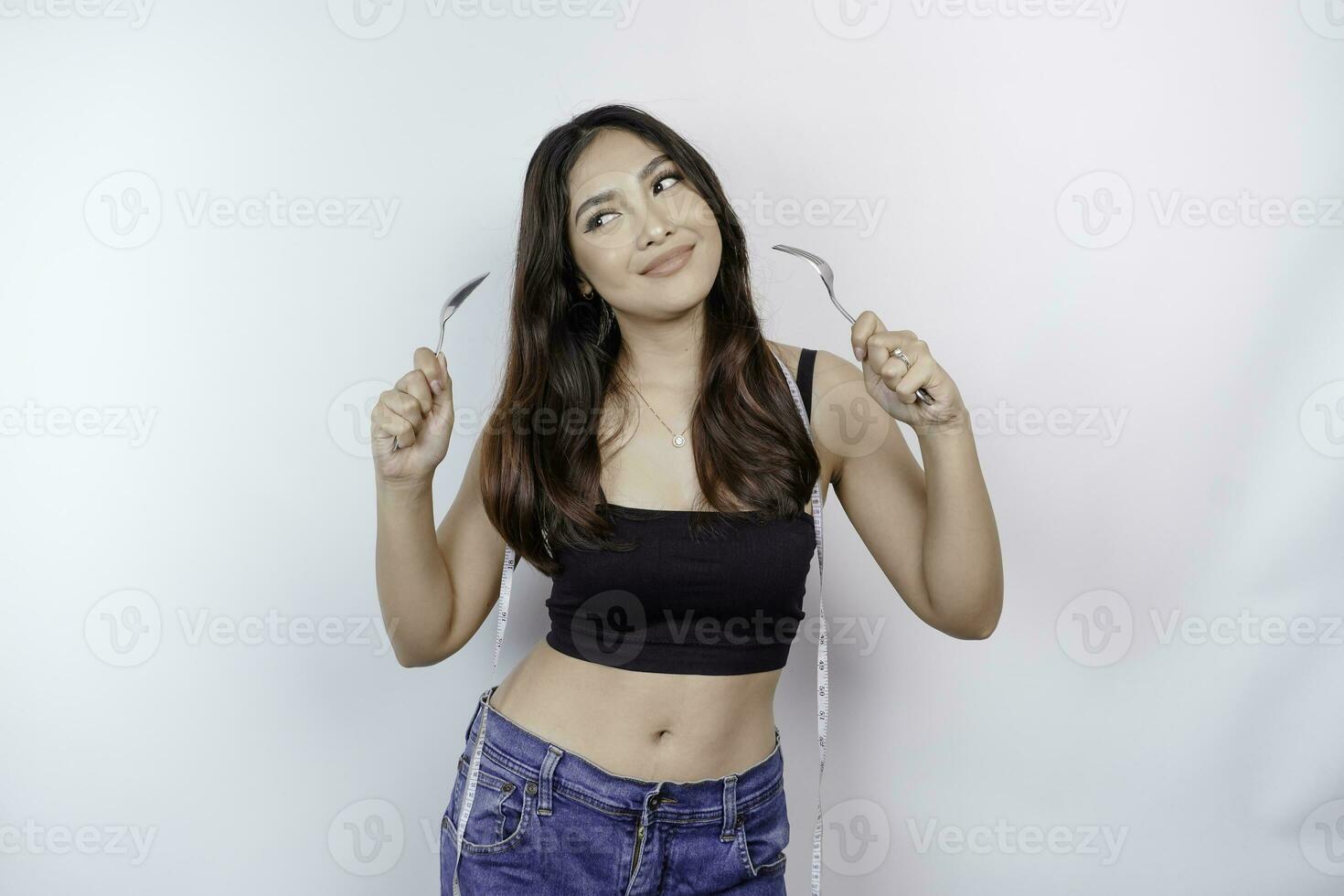 Portrait of happy young Asian woman wearing body measuring tape around waist holding spoon and fork isolated over white background photo