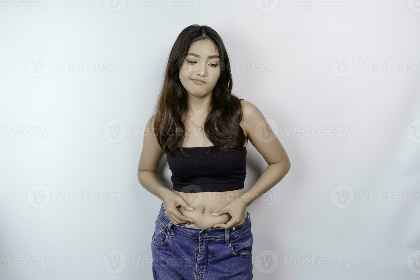 A sad young Asian woman pinching flabby skin fat belly isolated by white background photo