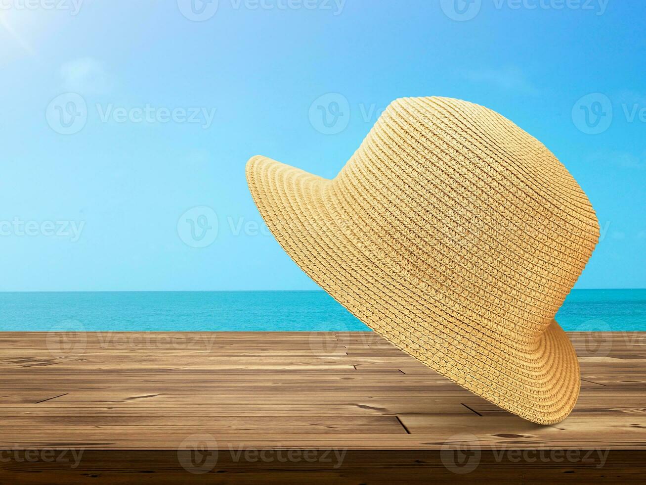 Straw hat laying on wooden table with sky and sea background. photo