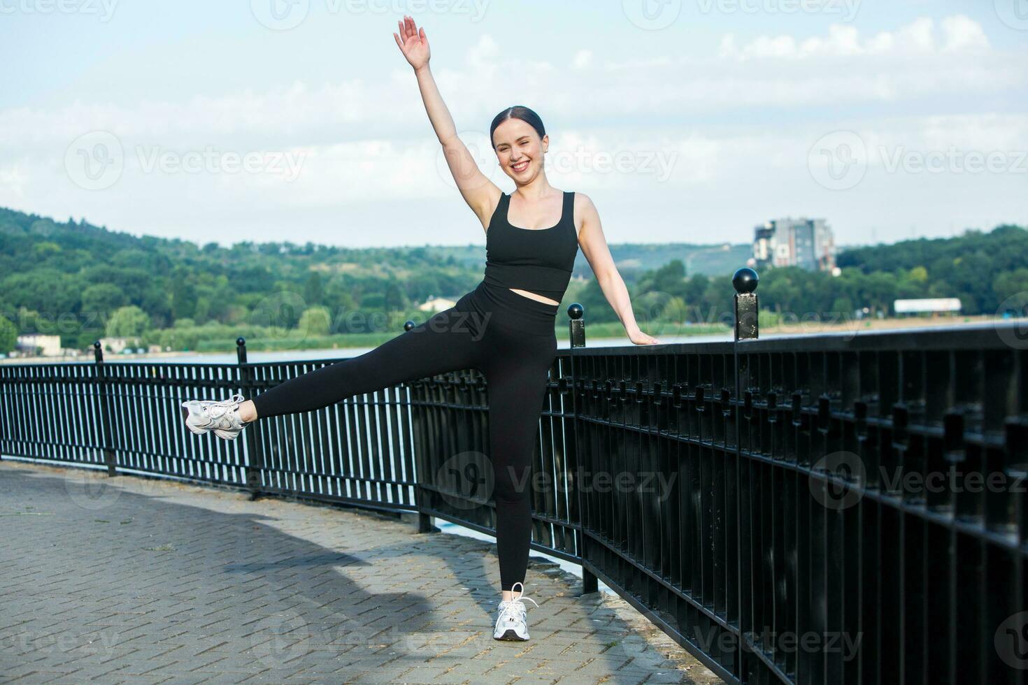 Portrait of smiling young woman in black sportswear exercising outdoors. Fitness and healthy lifestyle concept. photo