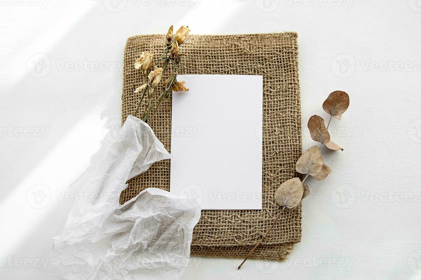 Fashionable white stock background with a blank postcard and flowers. Top view and copy space. photo