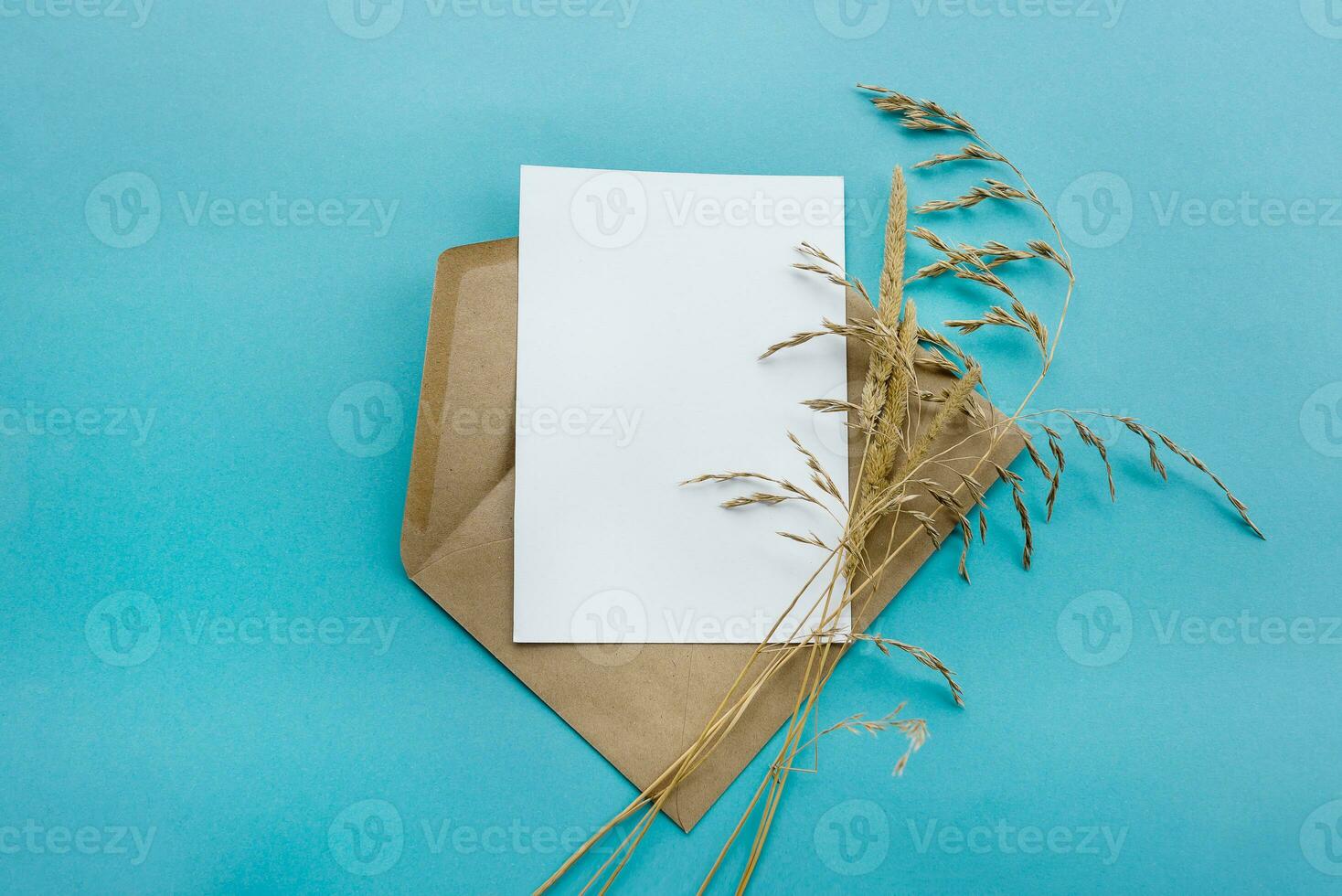 un Kraft papel sobre con un blanco blanco tarjeta flores en un azul antecedentes. tarjeta postal preparación foto