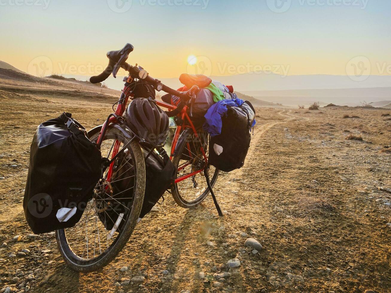 Loaded with bags red bicycle stands on side of road surrounded by mountains in countryside of VAshlovani national park. Bicycle touring holiday in Georgia photo