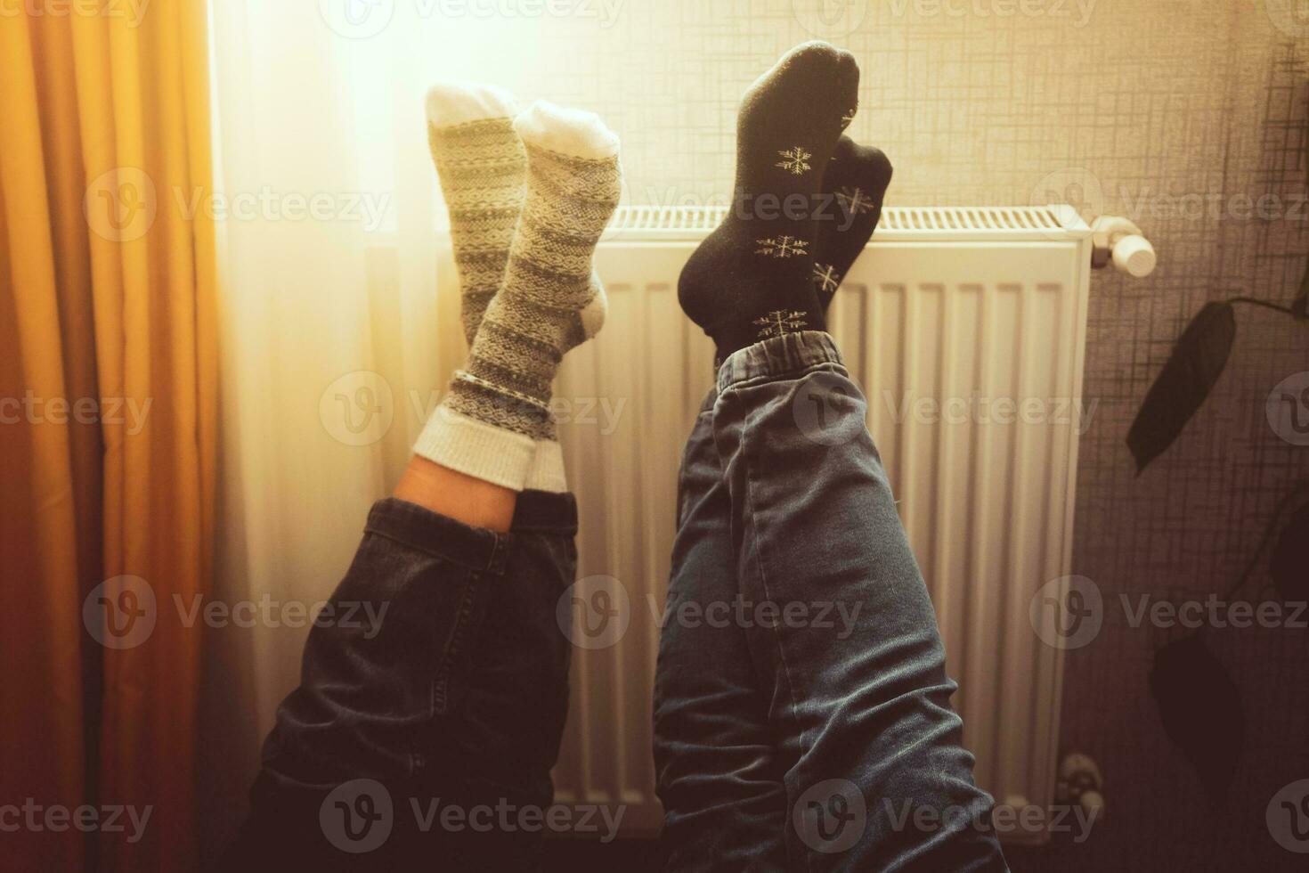 Couple hold legs up heating feet in cold home indoors on radiator in winter with cozy winter socks on. Valentines funny together warm feet by radiator by window photo