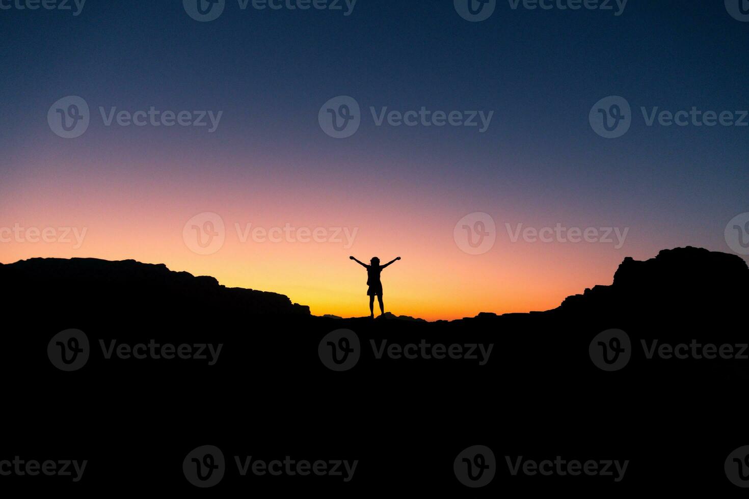 Silhouette of free cheering woman hiker open arms at mountaintop greet sunrise in Jordan desert of Wadi Rum photo