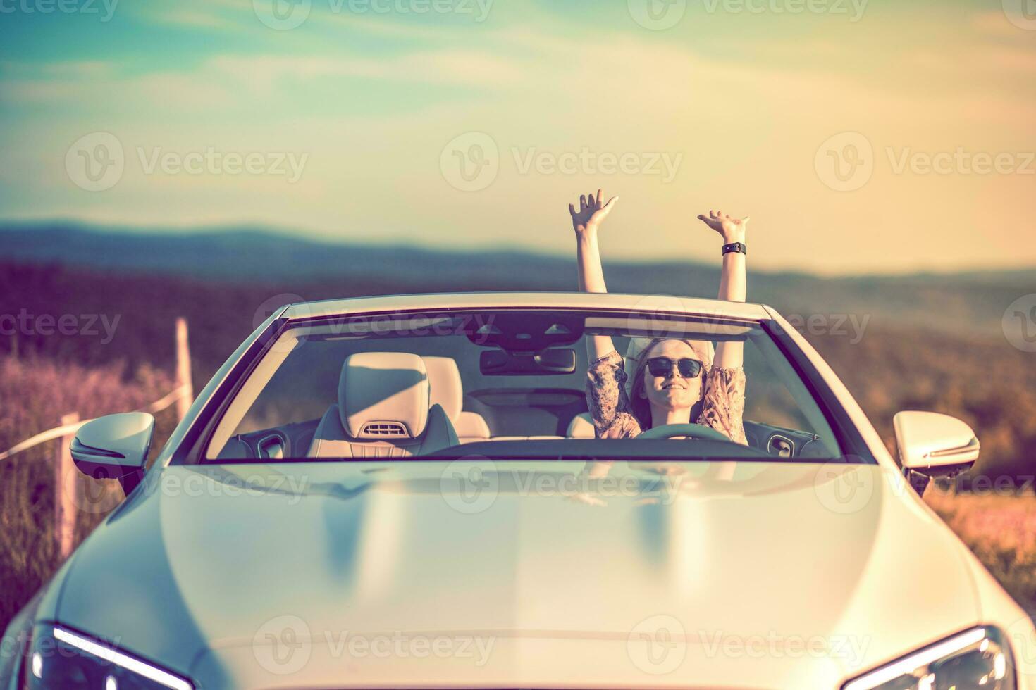 Happiness in a convertible. Young woman full of success with arms raised. Sunset. photo