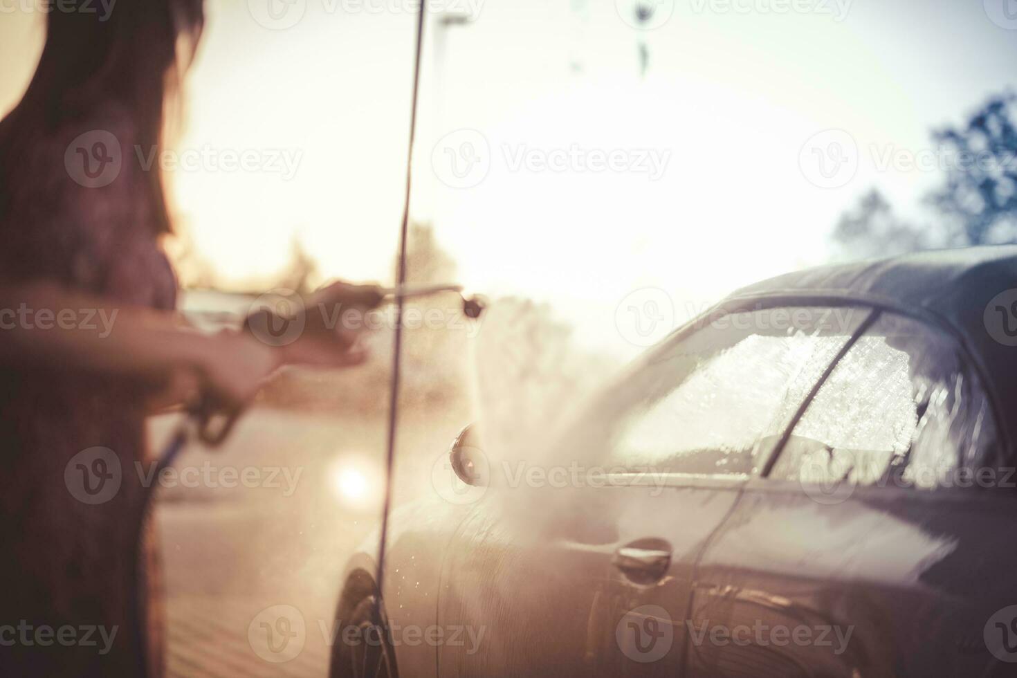 Woman washing her car during sunset. Self Car wash theme. photo